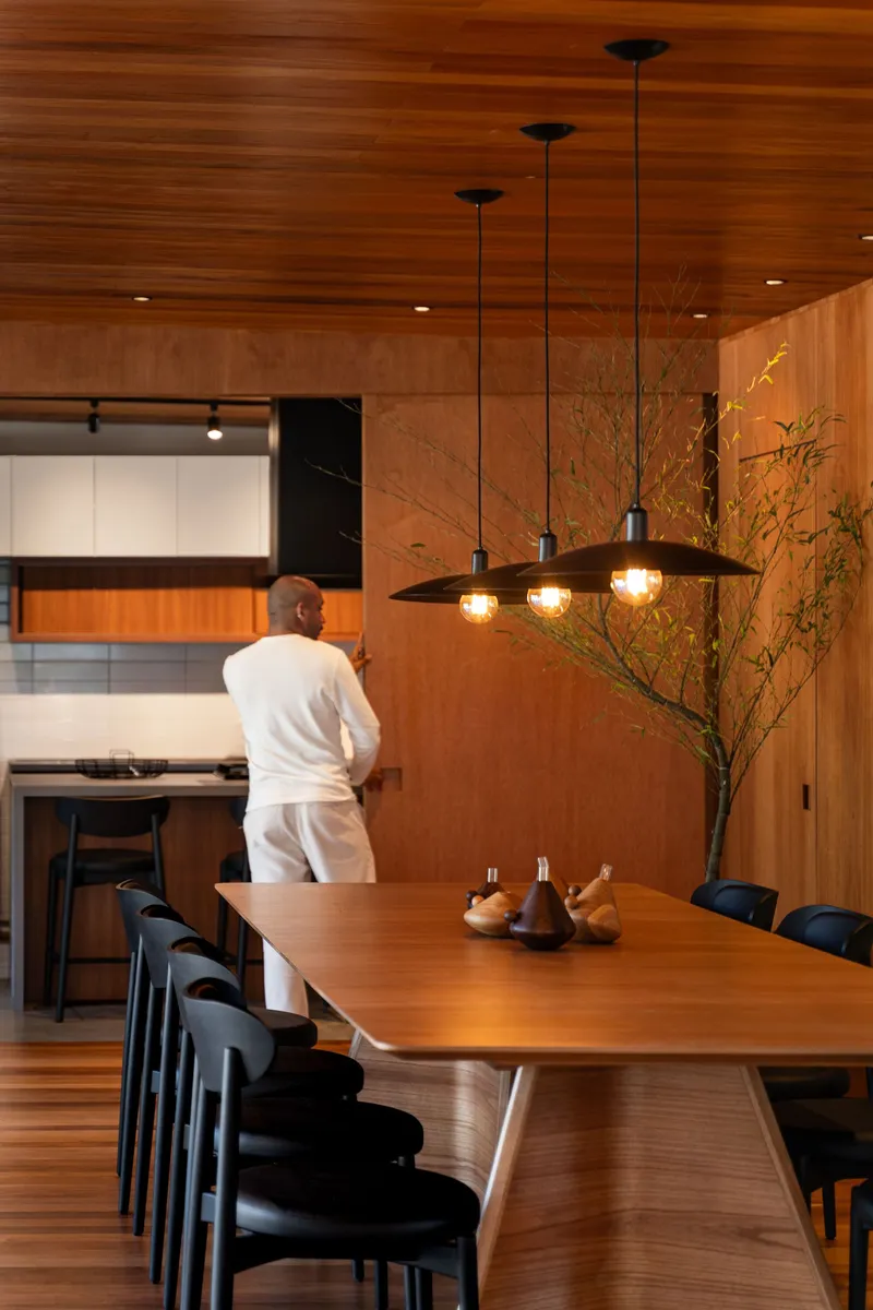 Dining area with timber table and three pendant lights suspended below a warm wood plank ceiling