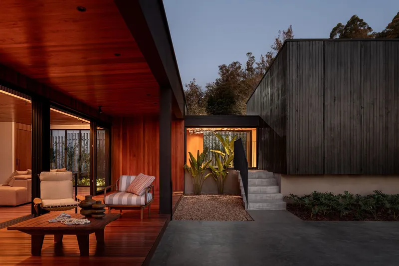 Courtyard view from timber deck showing concrete stairs and planters with person entering doorway at dusk