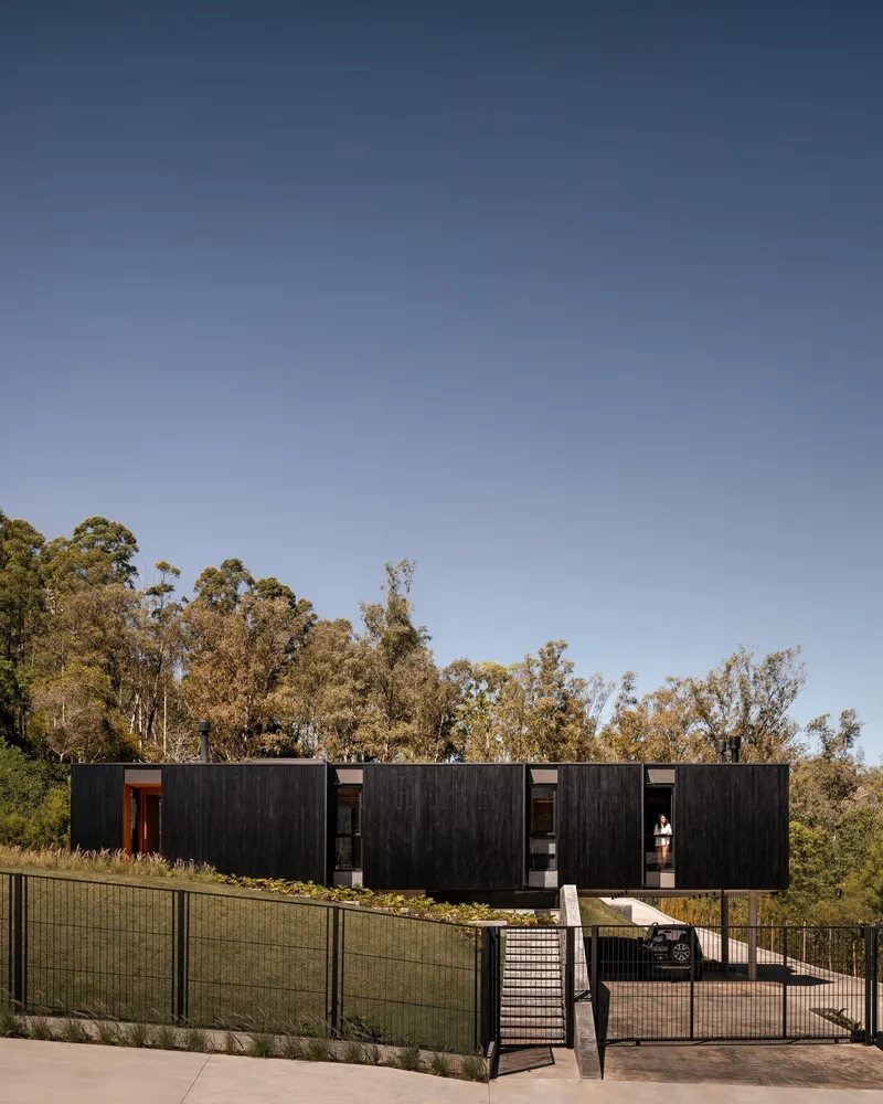 Elevated blackened wood facade with mesh fencing and concrete ramp under clear afternoon sky
