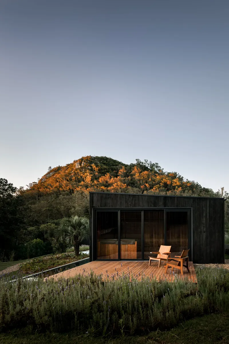 Timber deck with glazed openings and single chair facing illuminated hillside at dusk