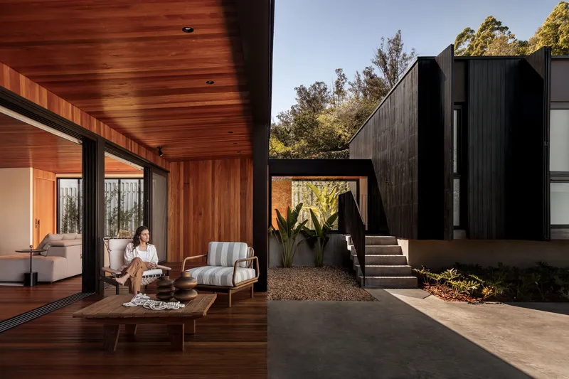 Covered terrace with timber ceiling and flooring opening to a gravel courtyard with black timber volumes beyond