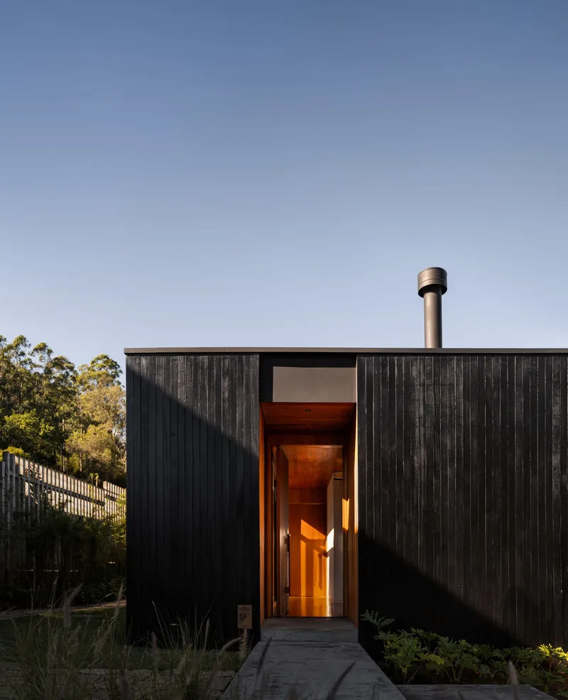 Front entry with vertical timber cladding and a warmly lit threshold at twilight