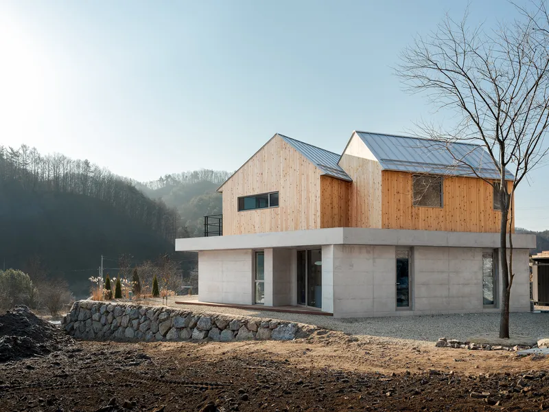 Twin gabled volumes with standing seam metal roofs resting on a board-formed concrete podium in morning mist