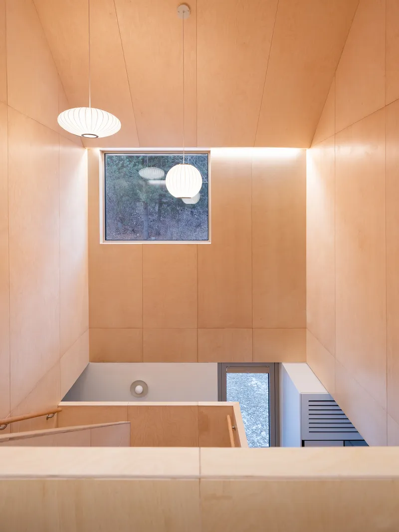 Looking down into plywood-lined double-height space with pendant light and square skylight overhead