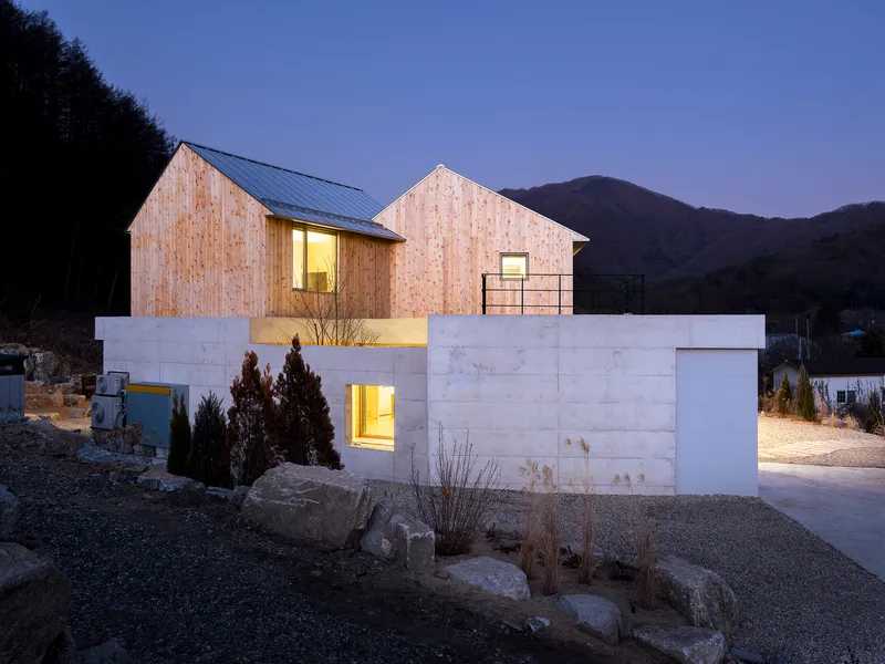 Evening view of illuminated windows glowing against timber facade and concrete base under dusky sky