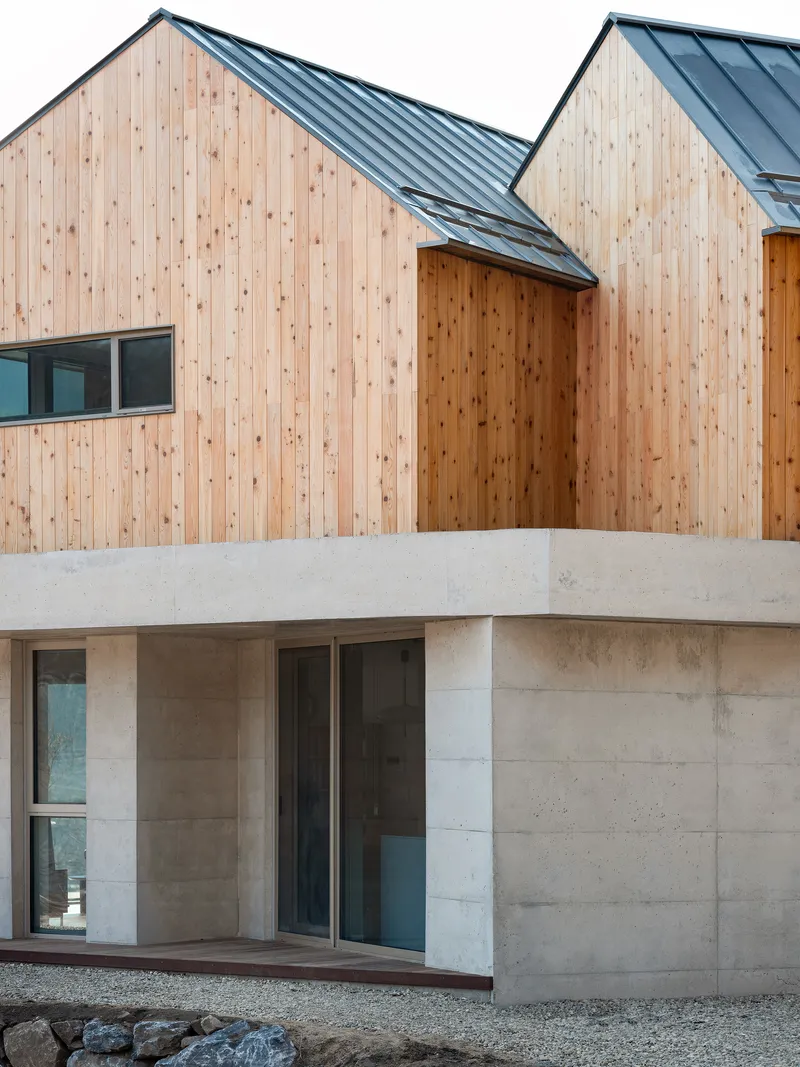 Two-level facade combining vertical timber cladding above and board-formed concrete below with gravel courtyard