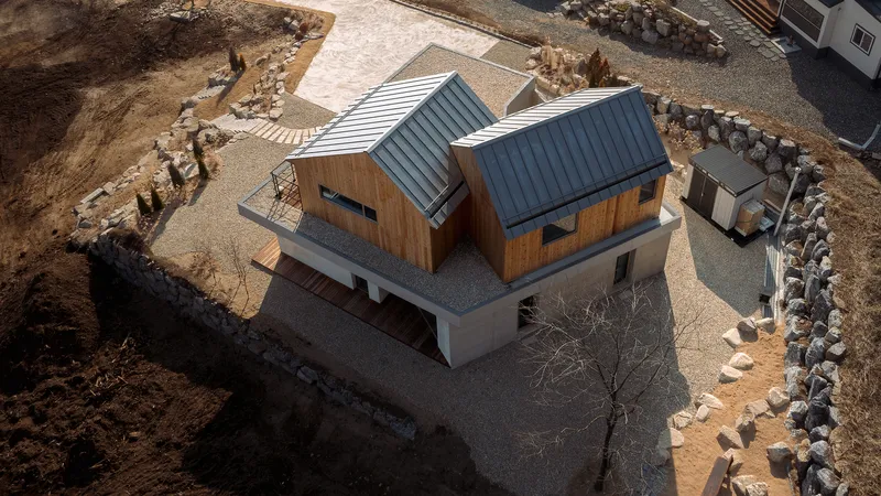 Drone view of the two gabled volumes with metal roofs sitting on a concrete plinth