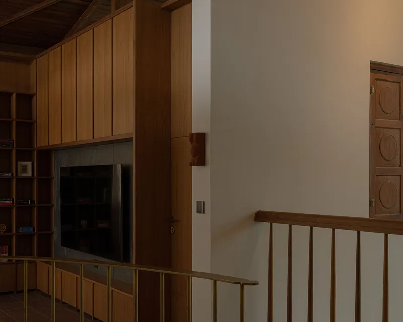 Timber staircase railing beside a built-in cabinetry wall with recessed television niche in dim light