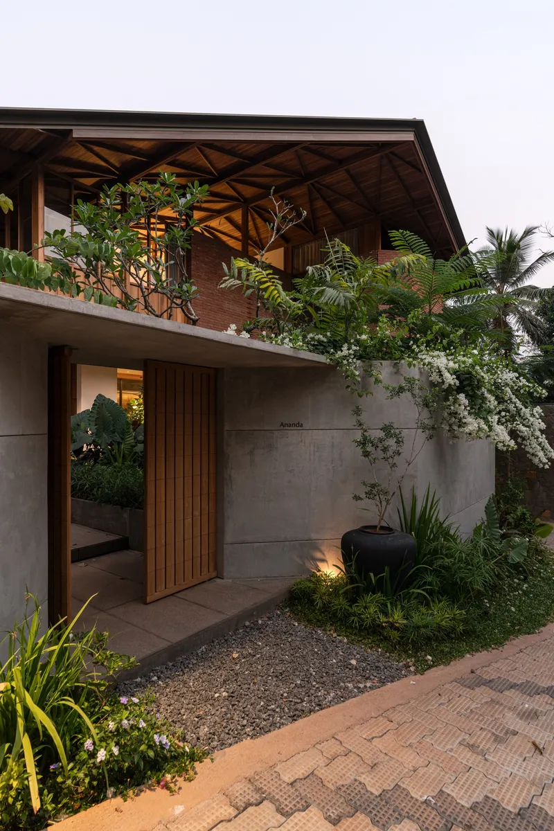Concrete entrance wall with timber slat door and planted terrace balcony above at dusk