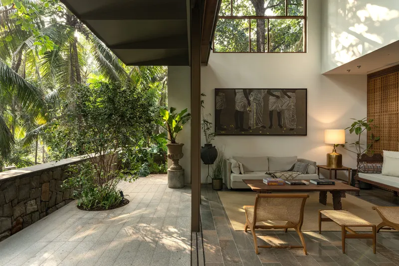 Double-height living space opening to planted terrace with afternoon light filtering through tree canopy