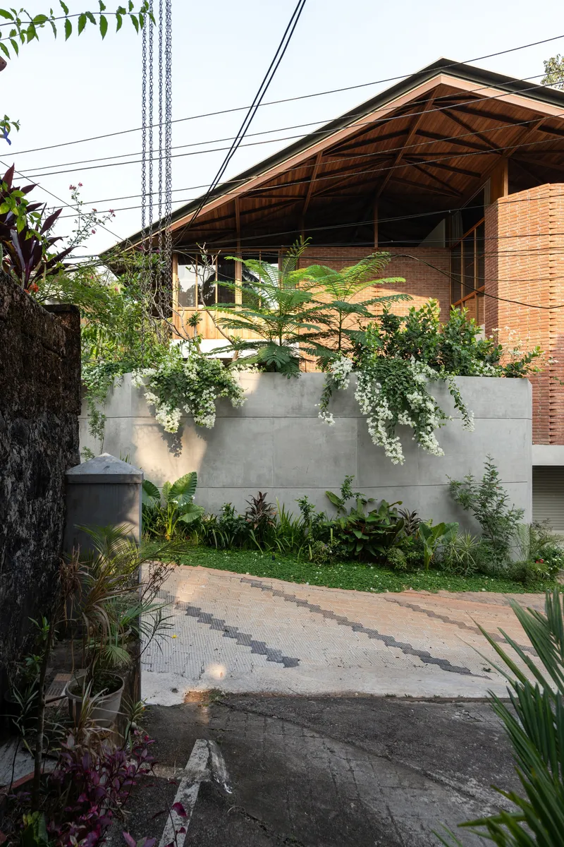 Street view of the pitched roof structure with brick walls and planted concrete boundary wall