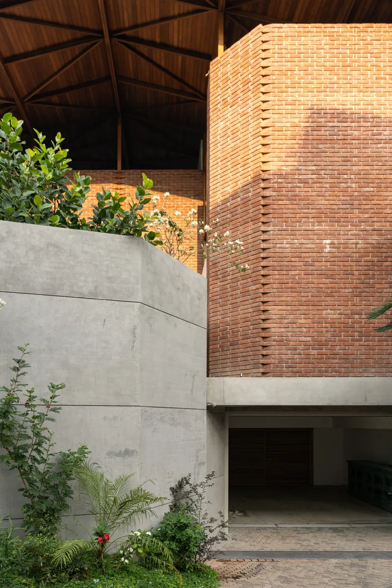 Concrete planter wall meeting brick volume with recessed garage opening beneath exposed timber roof