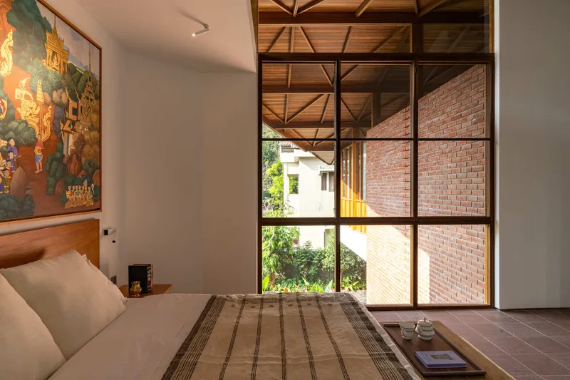Bedroom with steel-framed glazing opening to an adjacent brick volume under an exposed timber truss ceiling