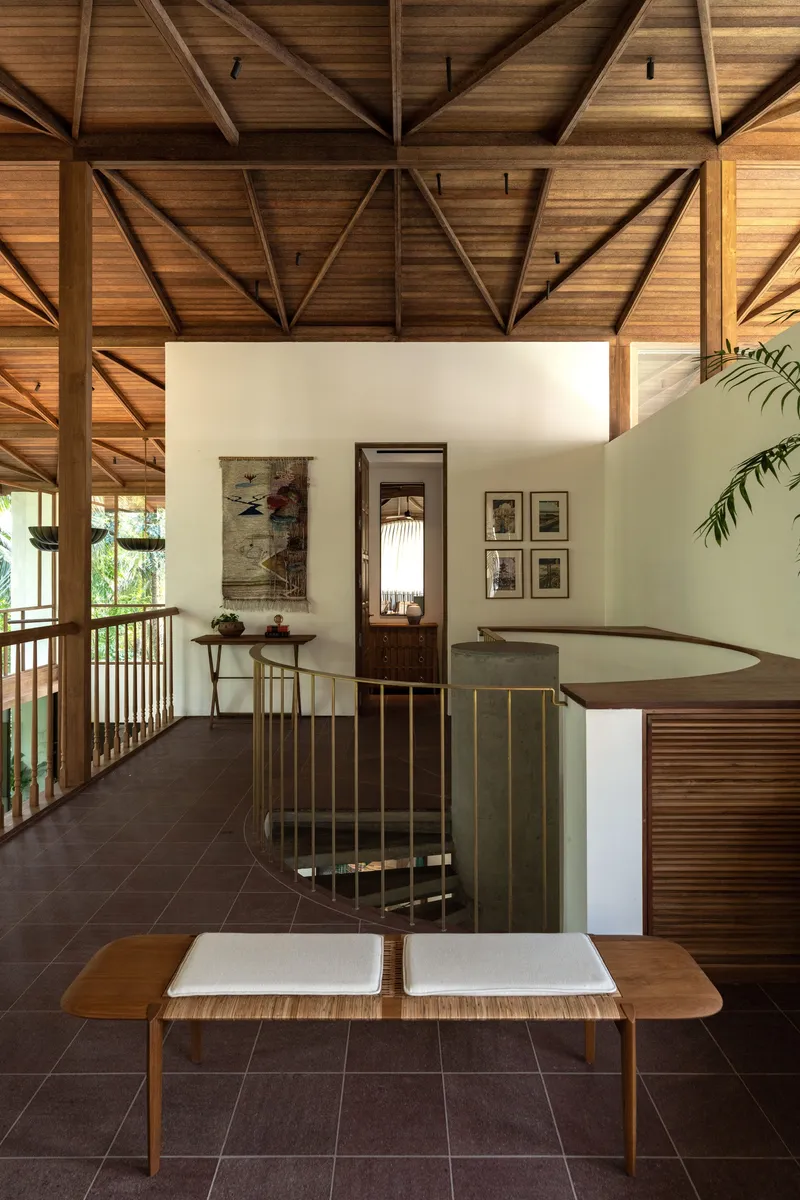 Upper-level landing with brass spiral stair and exposed timber ceiling structure in afternoon light