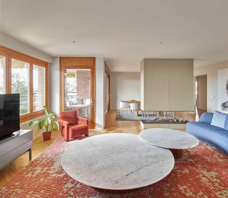 Living room with vertically fluted fireplace wall, marble coffee tables, and timber-framed windows overlooking greenery