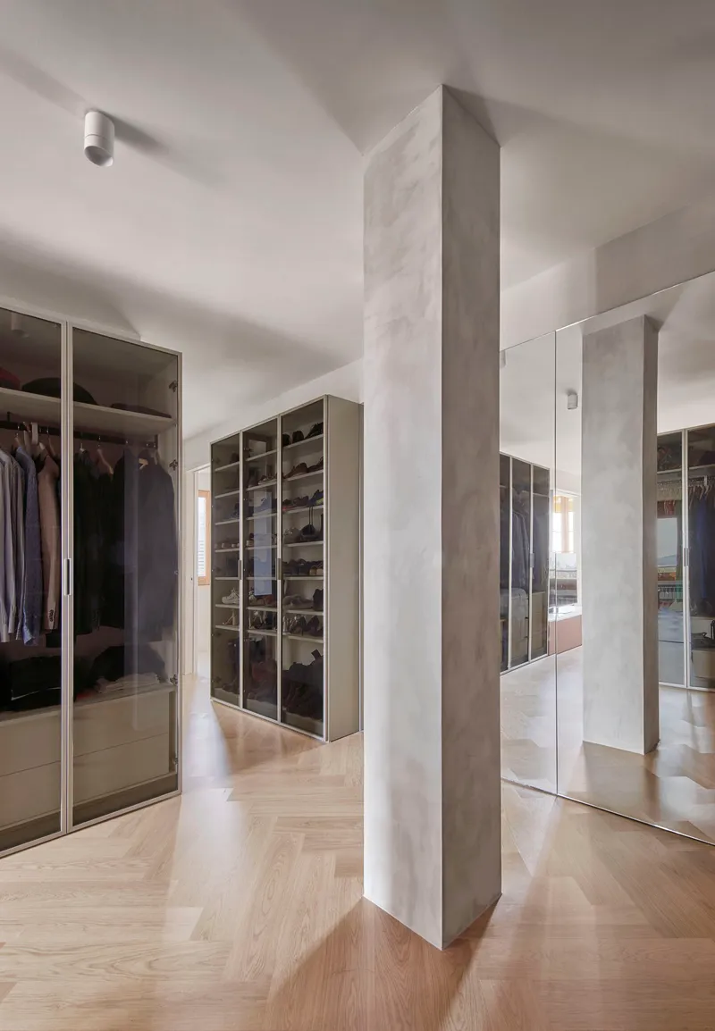 Dressing room with mirrored wardrobes and freestanding terrazzo-clad column on herringbone oak flooring