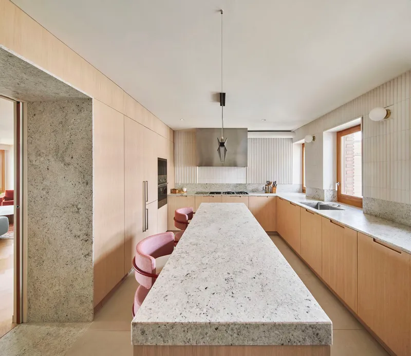 Galley kitchen with terrazzo island, oak cabinetry, fluted wall panels, and stainless steel range hood