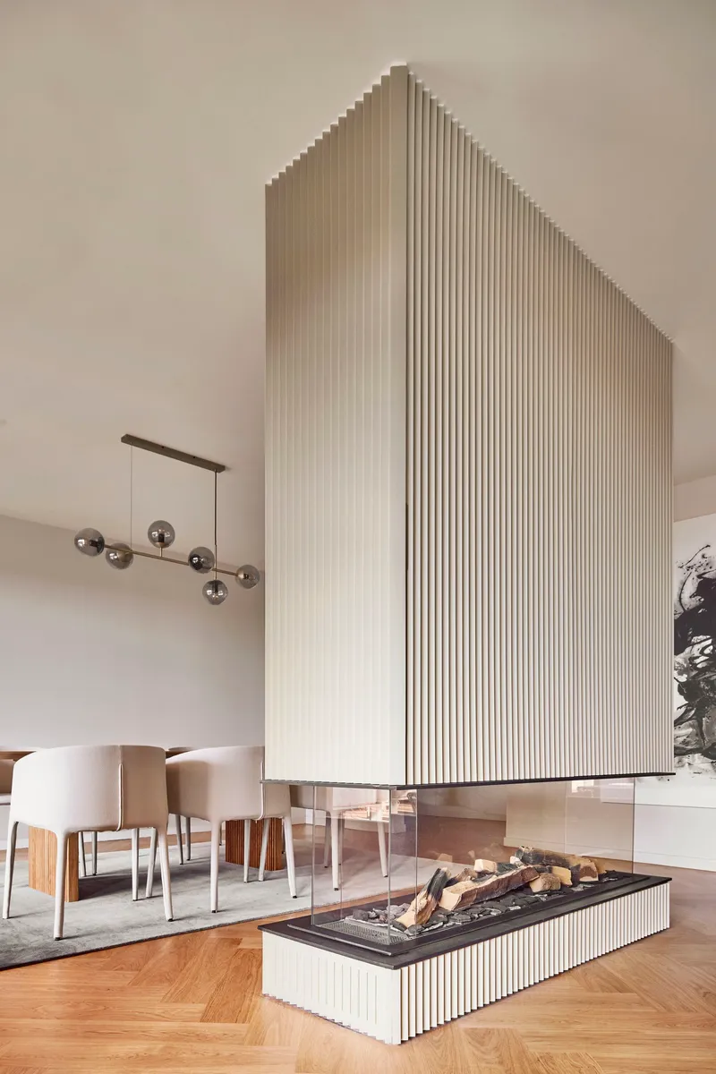 Fluted white fireplace column with black hearth and stacked firewood below a bronze pendant lamp