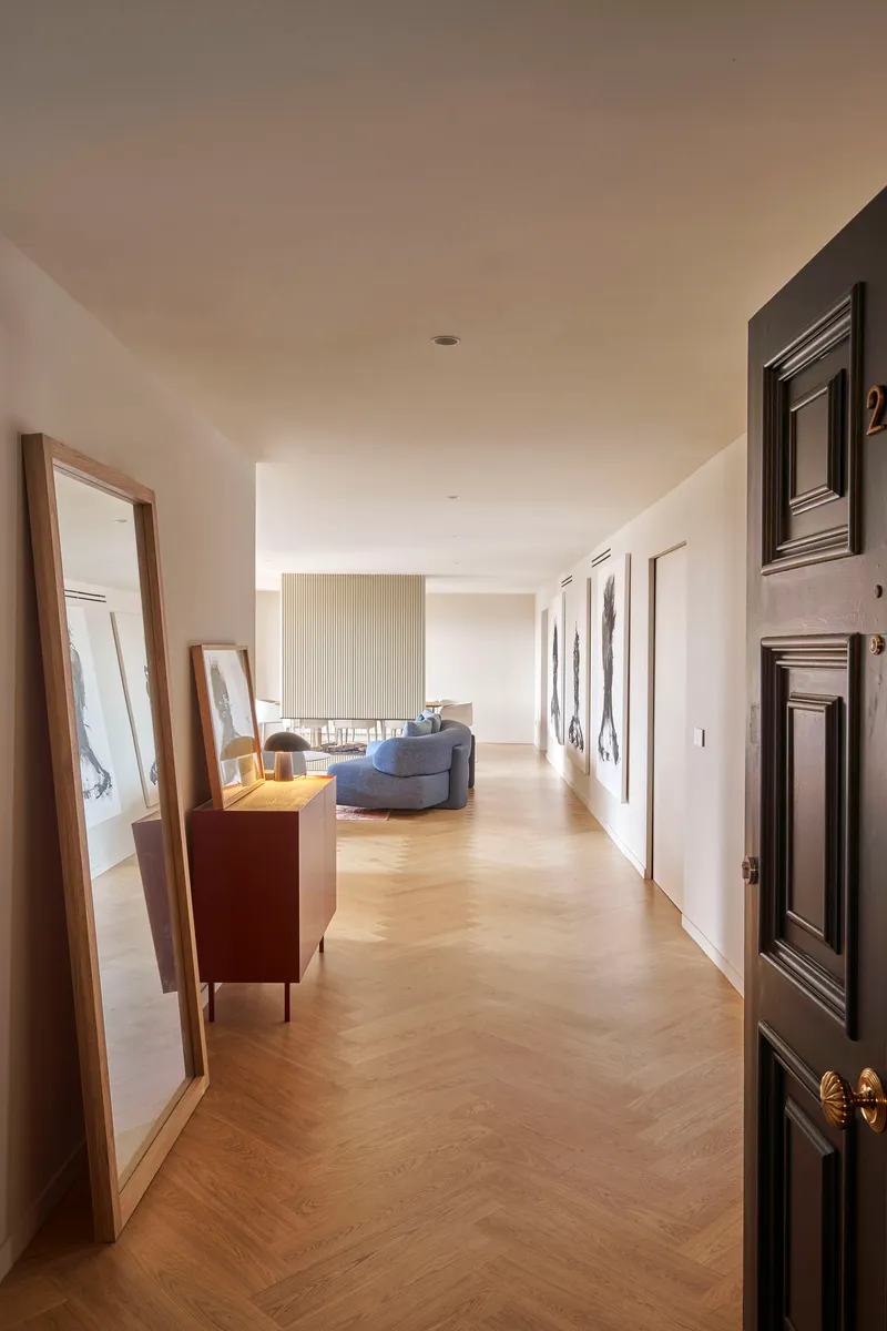 Long hallway with chevron parquet flooring and framed artwork leading to a seating area