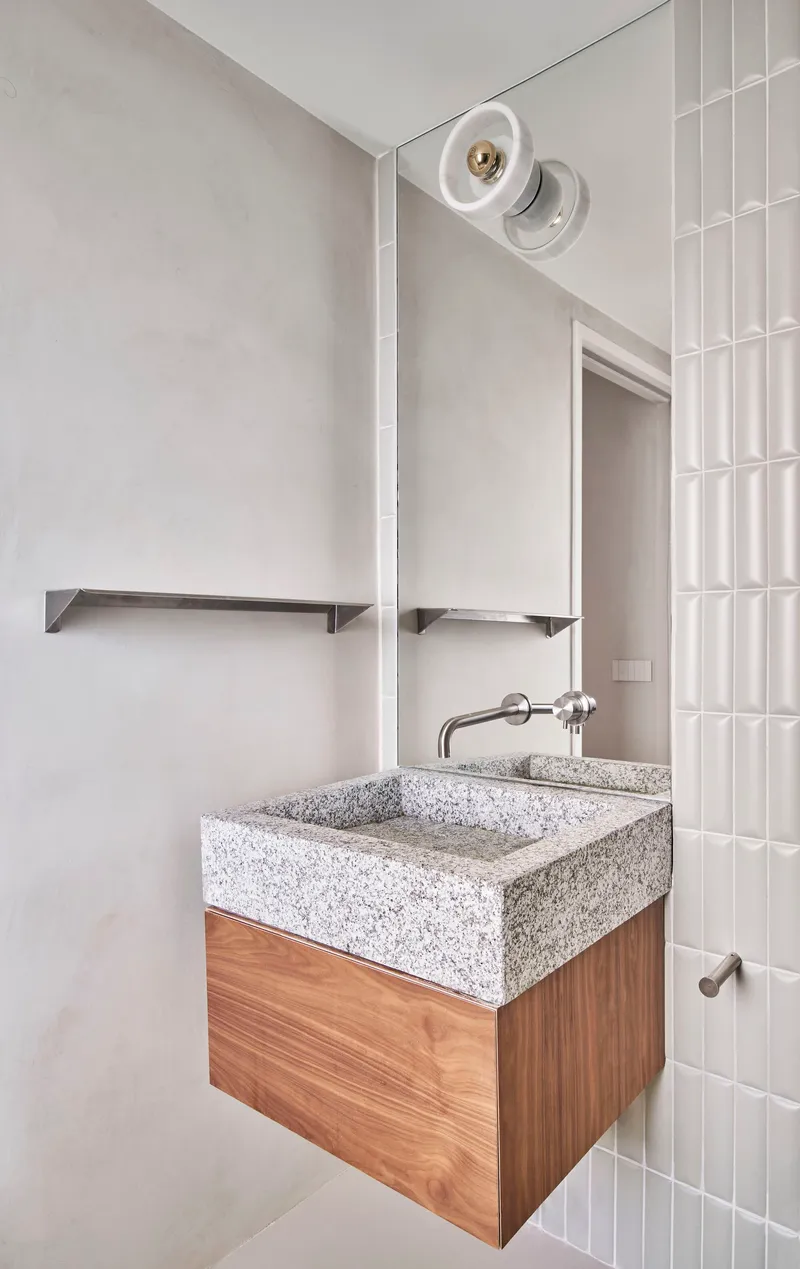Bathroom vanity with terrazzo sink on timber cabinet beside vertical white tile wall