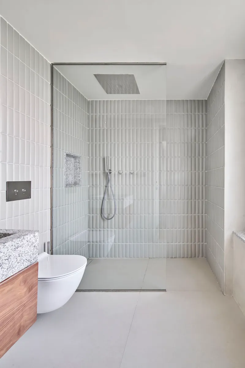 Glass-enclosed shower with vertical white tile walls and ceiling-mounted rainfall showerhead