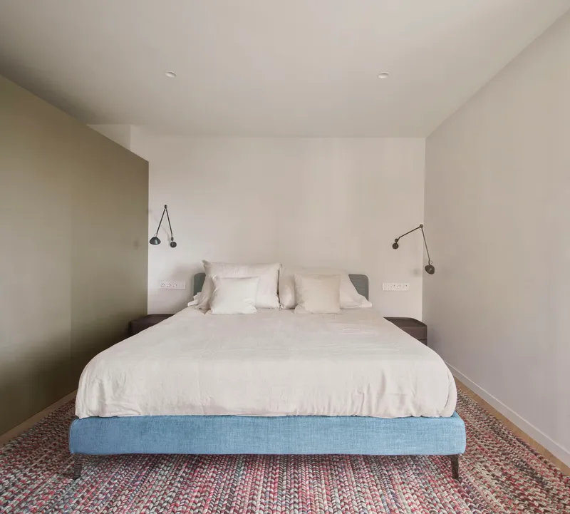 Bedroom with blue upholstered platform bed and articulated wall-mounted reading lamps