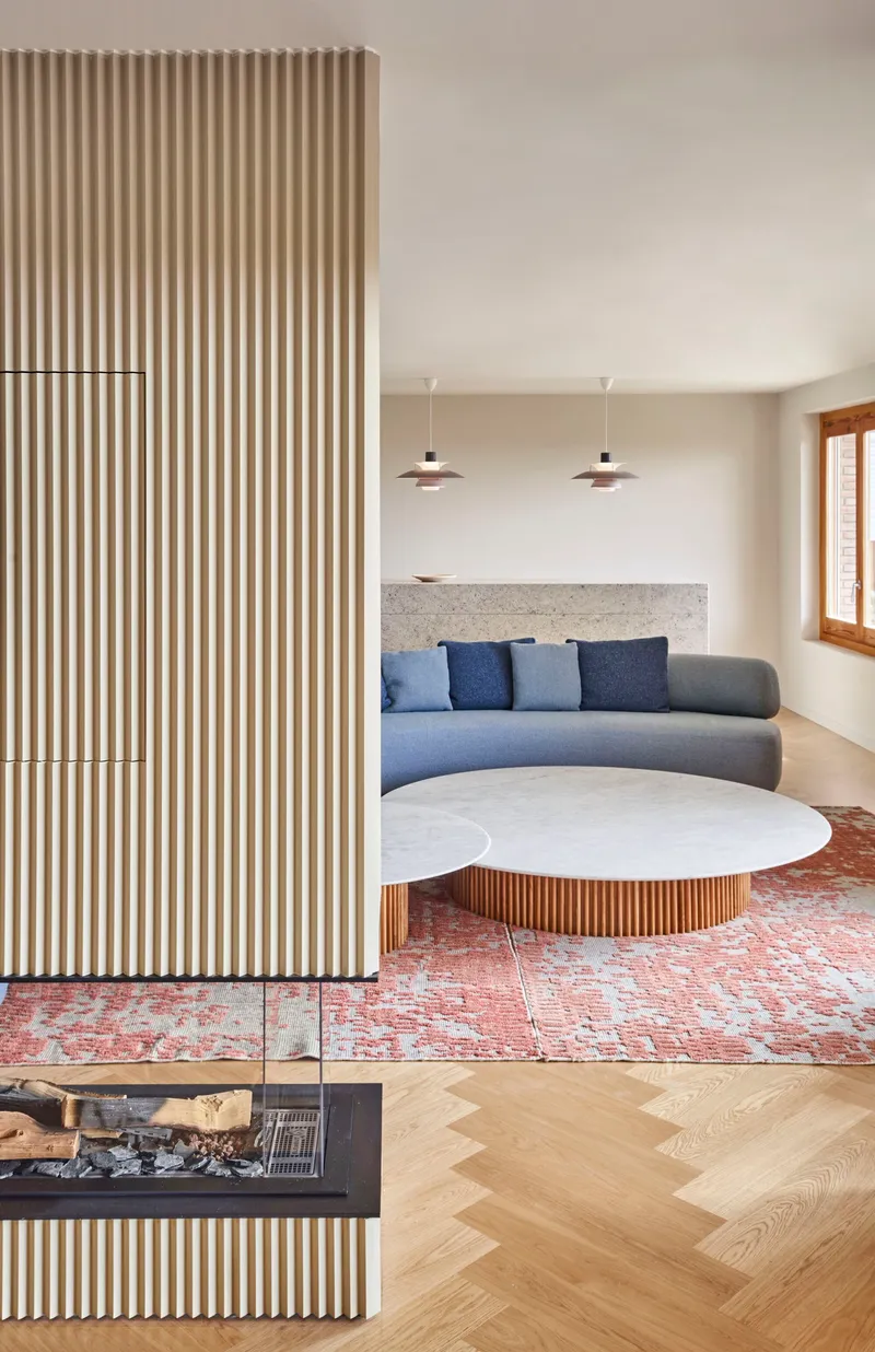 Living room with vertical fluted timber partition, curved sofa, and herringbone oak flooring over patterned rug