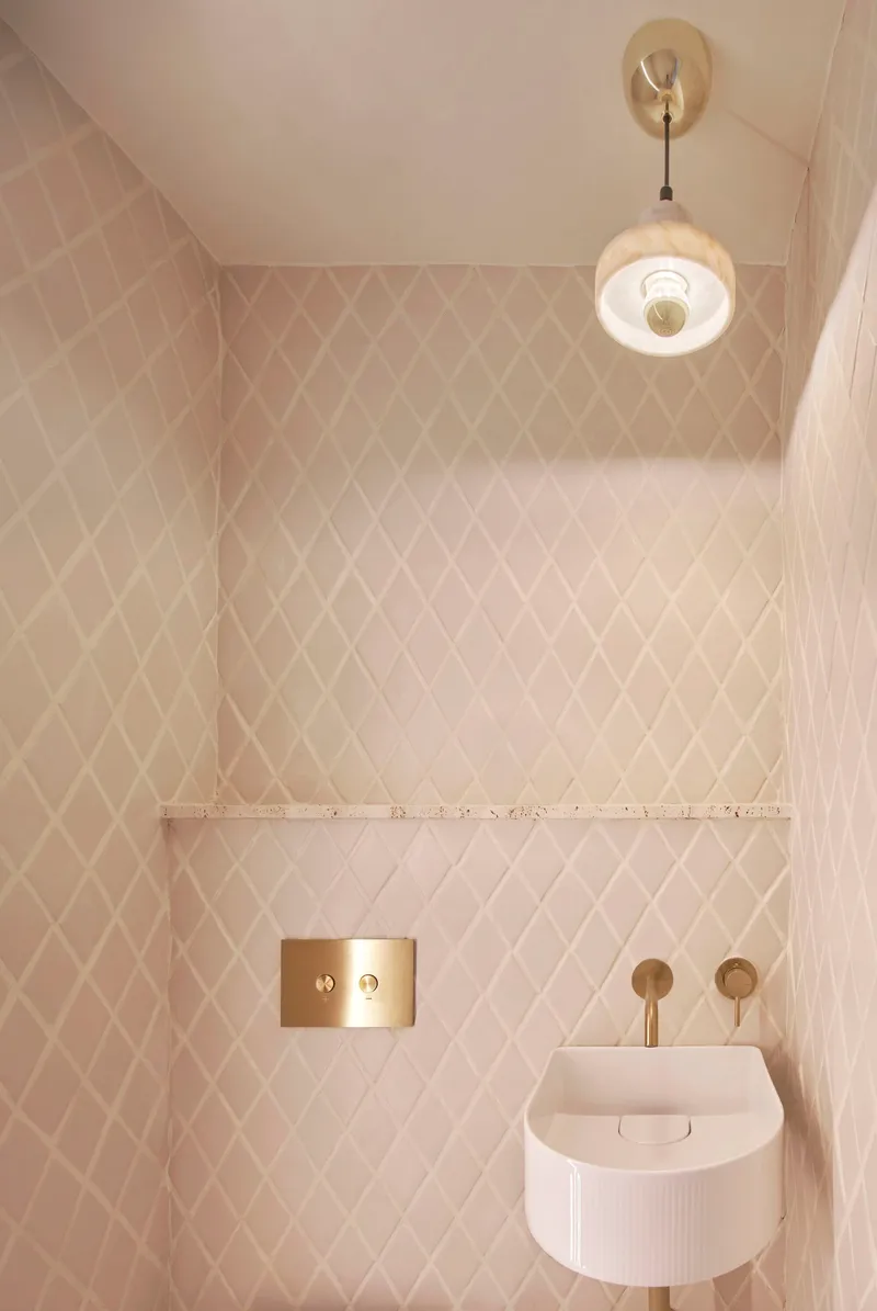 Compact bathroom with diamond-pattern tile walls, brass fixtures, and ribbed wall-mounted sink below pendant light