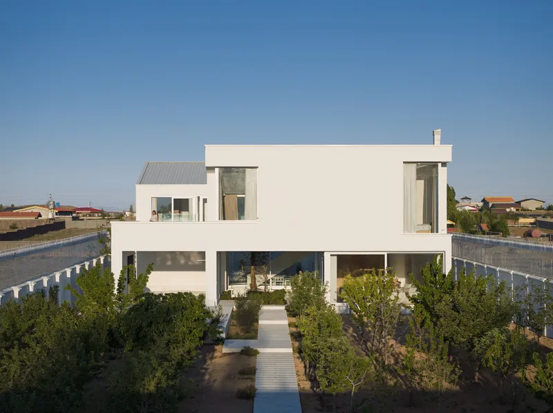 White rendered facade with recessed balcony and planted garden with olive trees under clear sky