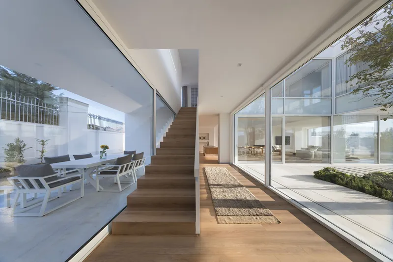 Timber staircase ascending beside floor-to-ceiling glazing overlooking a courtyard with outdoor seating