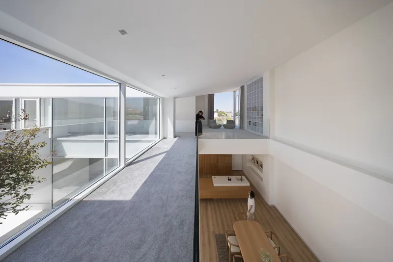 Upper-level corridor with a glass guardrail overlooking the dining area below and a courtyard garden