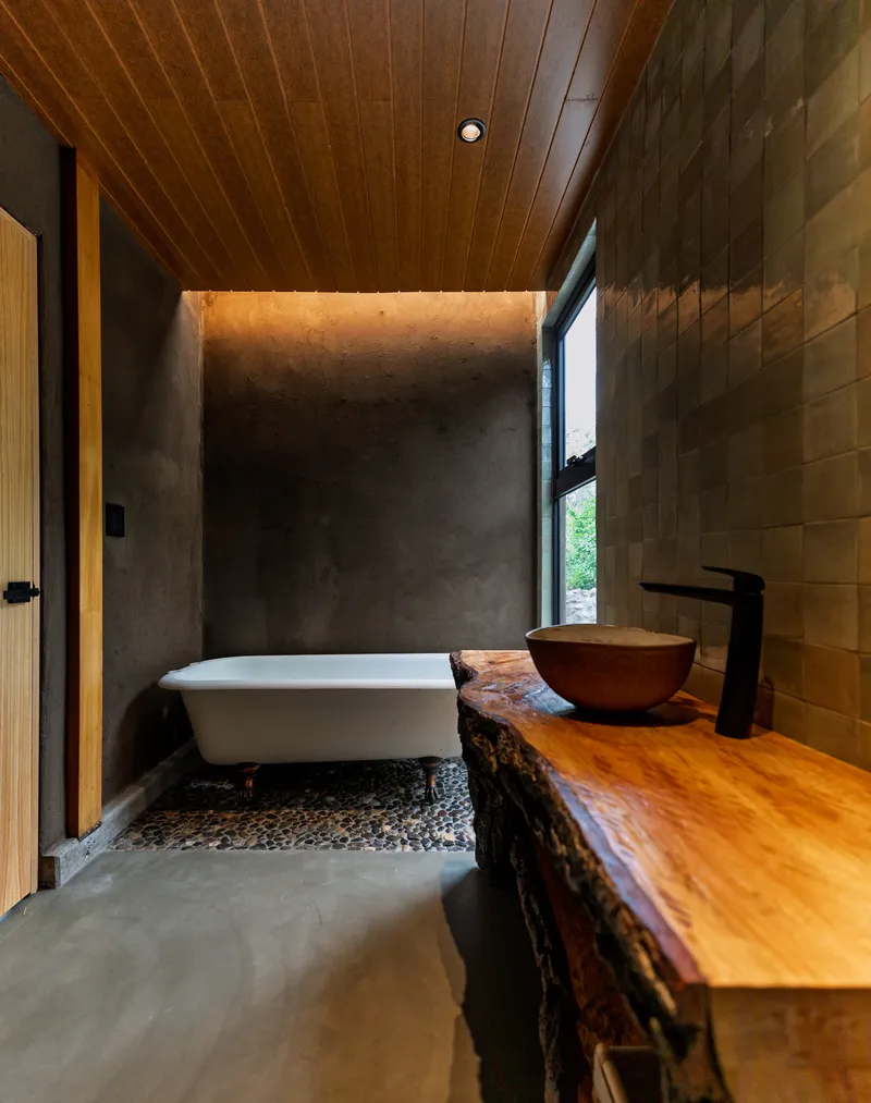 Bathroom with freestanding tub on river stones and live-edge wood vanity beneath wood plank ceiling