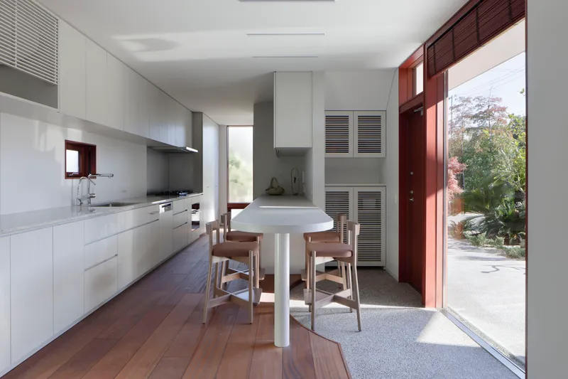 Galley kitchen with white cabinetry and timber table opening to courtyard through mahogany-framed doors