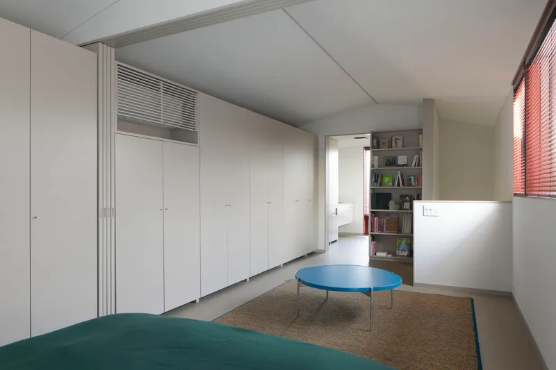 Bedroom with wall of white closets and terrazzo flooring under venetian-blinded window