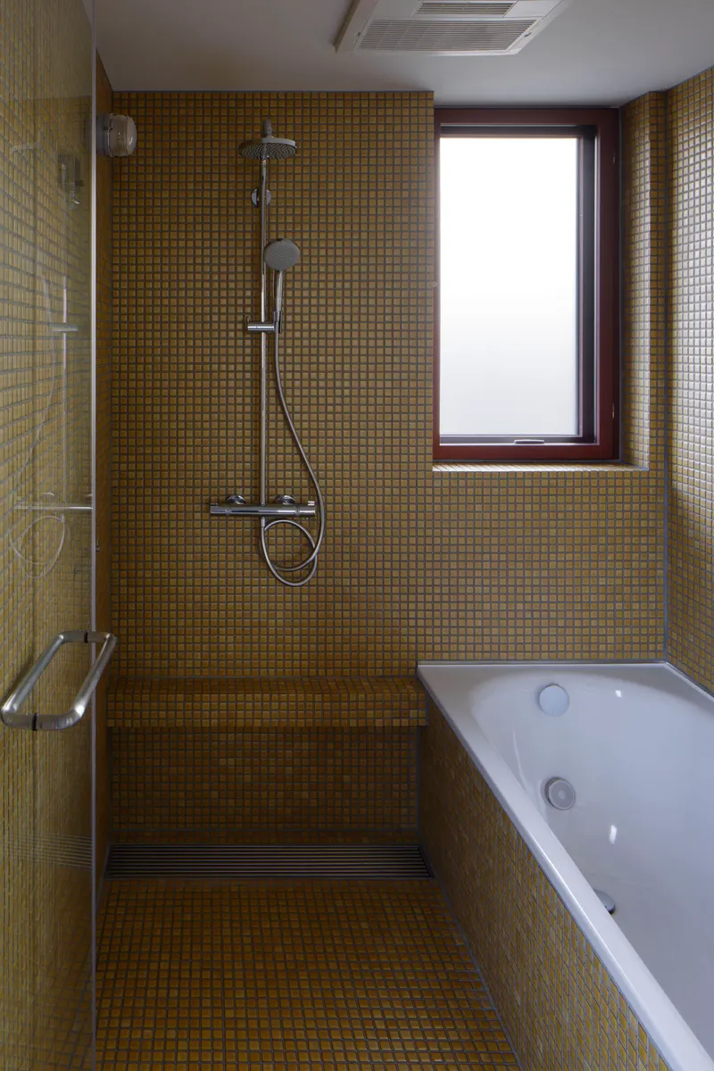 Bathroom interior with golden mosaic tile walls, walk-in shower, white bathtub and frosted window