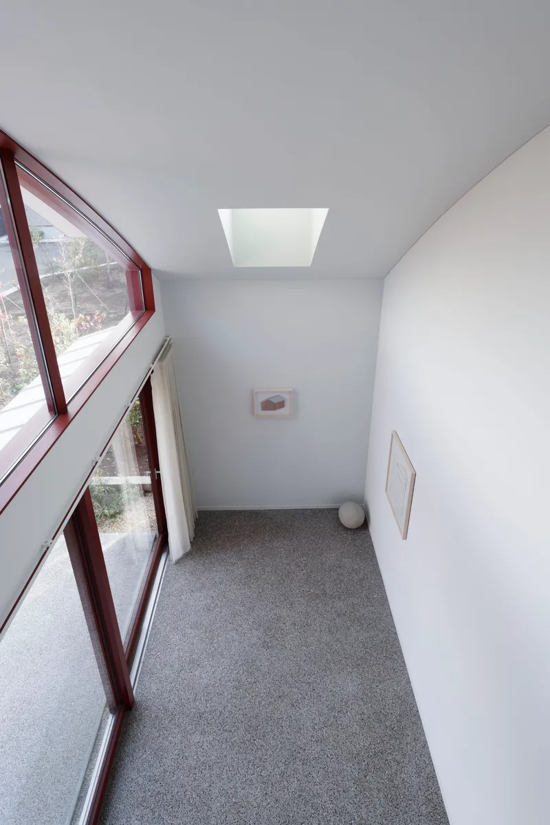 Narrow hallway with angled glazing, terrazzo flooring, white walls and central skylight above