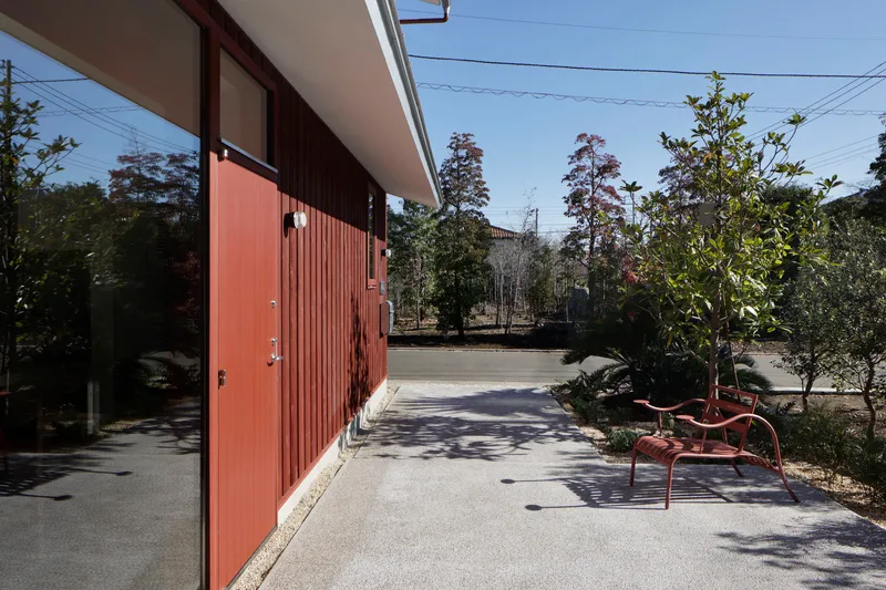 Courtyard with vertical timber cladding, concrete paving, planted trees and red bench in dappled shade