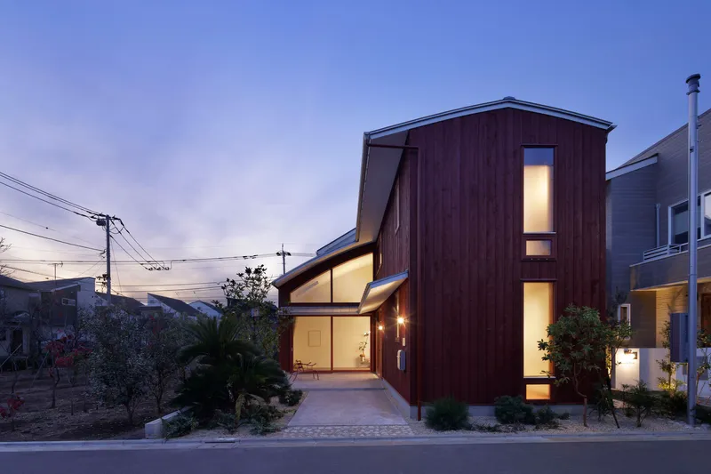 Street view of timber-clad volumes with illuminated glazing and planted front garden at dusk