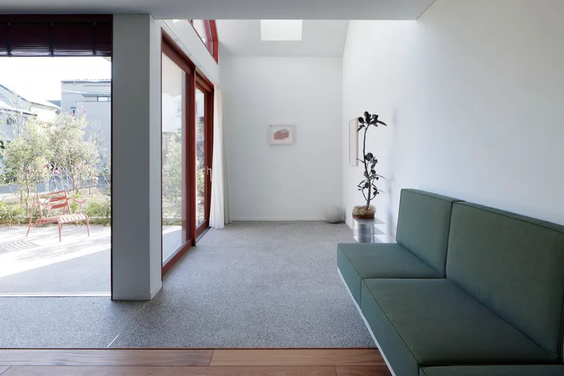 Interior living space with terrazzo floor, green sofa and glass doors opening to planted courtyard