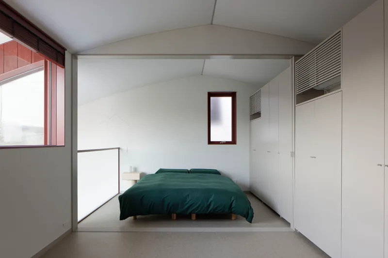 Bedroom with vaulted ceiling, built-in wardrobes and narrow vertical window framing distant view