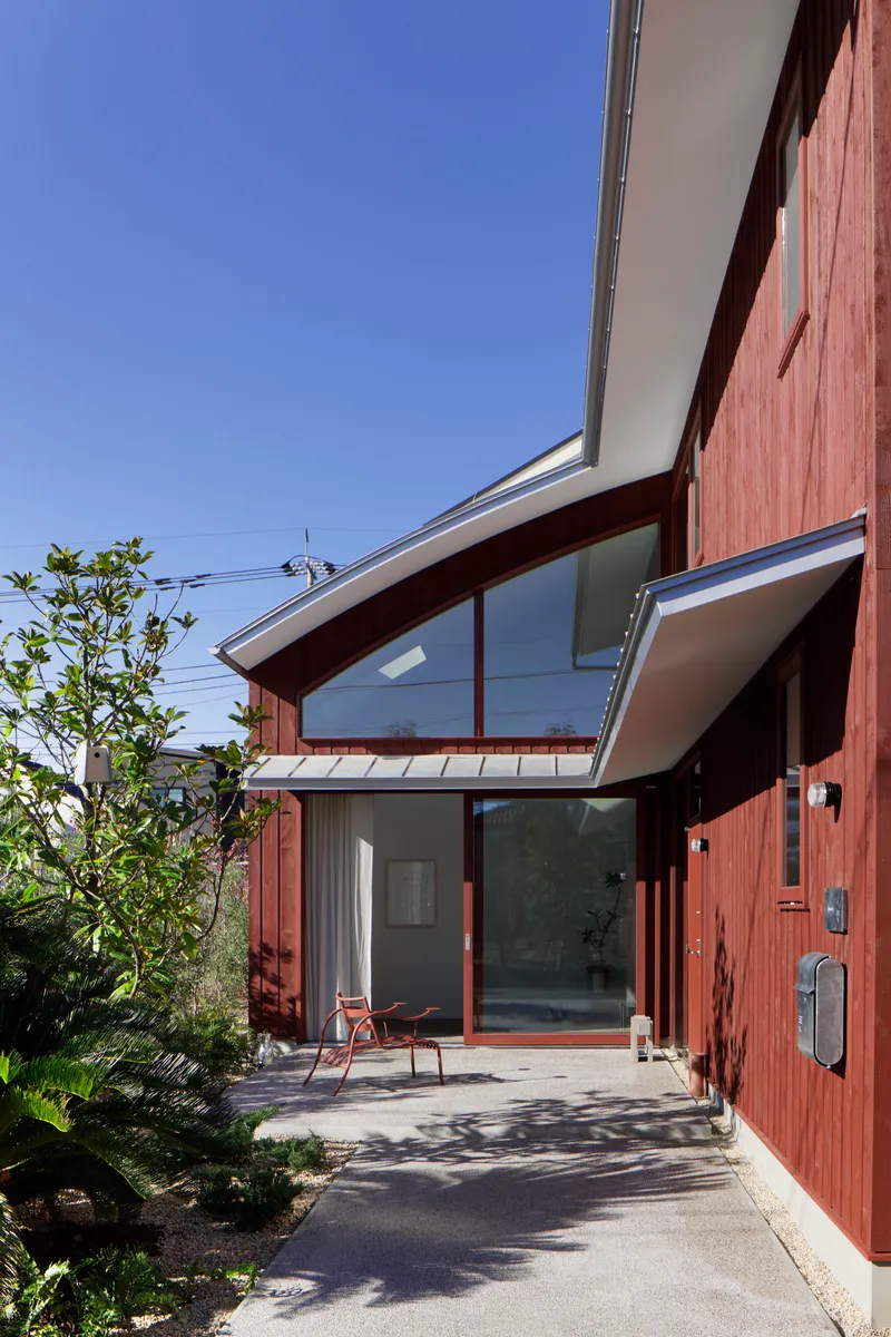 Entry porch with curved glazed roof and concrete path casting shadows under clear sky
