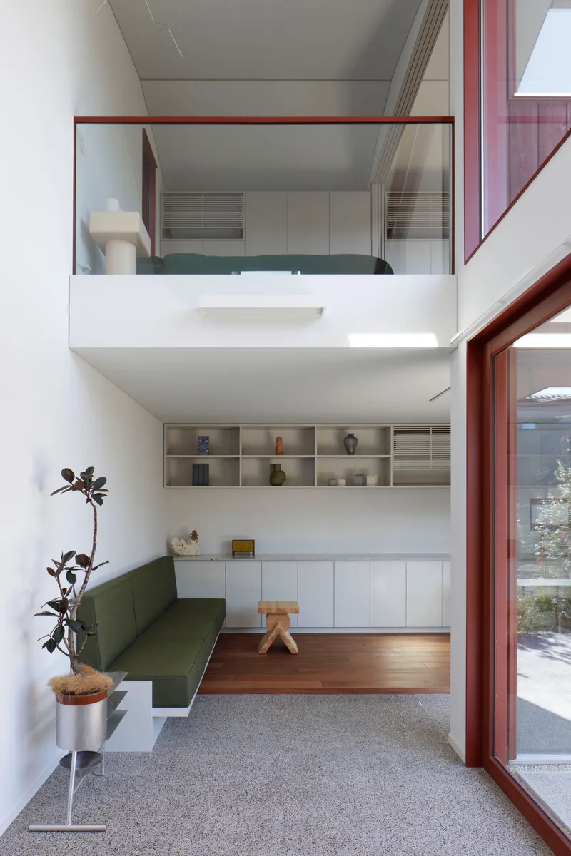 Double-height living space with mezzanine study overlooking built-in seating and open shelving below