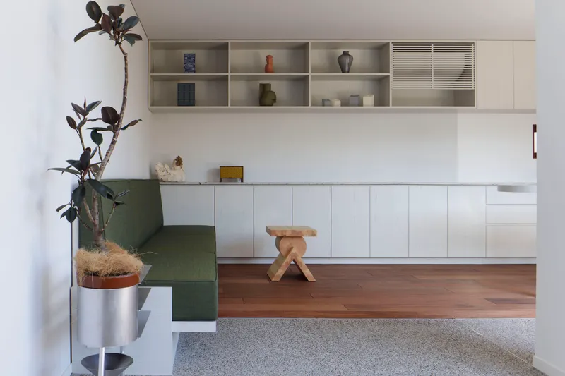 Built-in bench with green upholstery beside timber step-up platform and wall-mounted shelving unit
