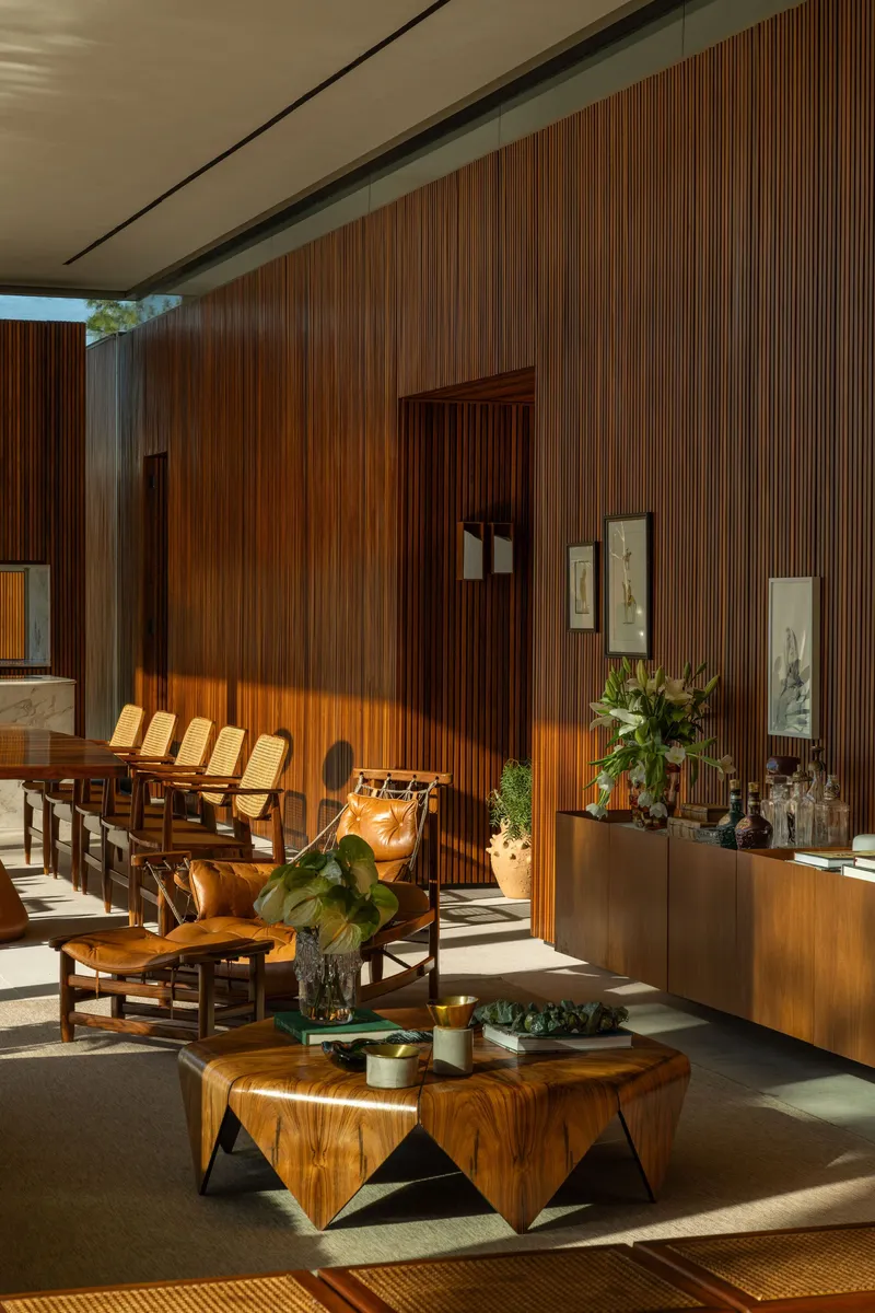 Living room with vertical timber wall panels illuminated by afternoon sunlight through floor-to-ceiling glass