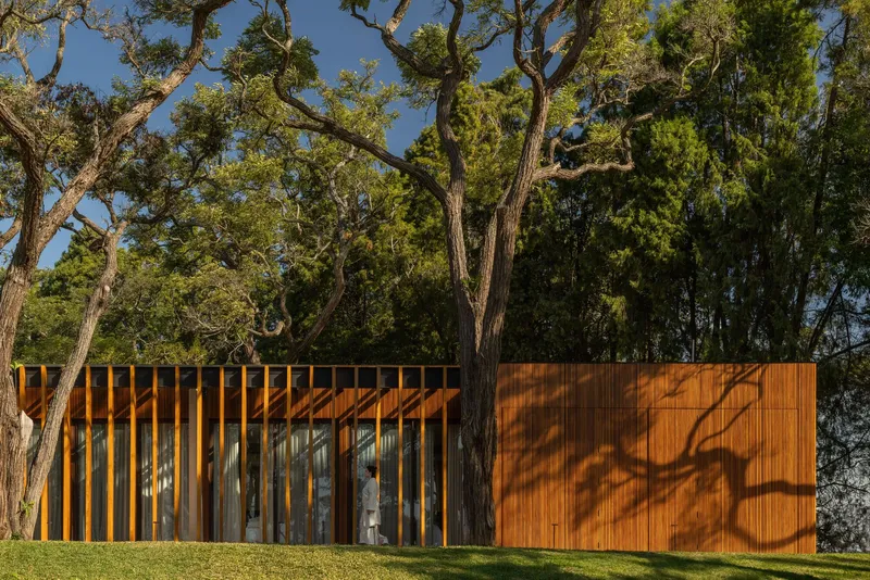Timber screen wall with vertical slats and solid panels beneath trees casting dappled shadows