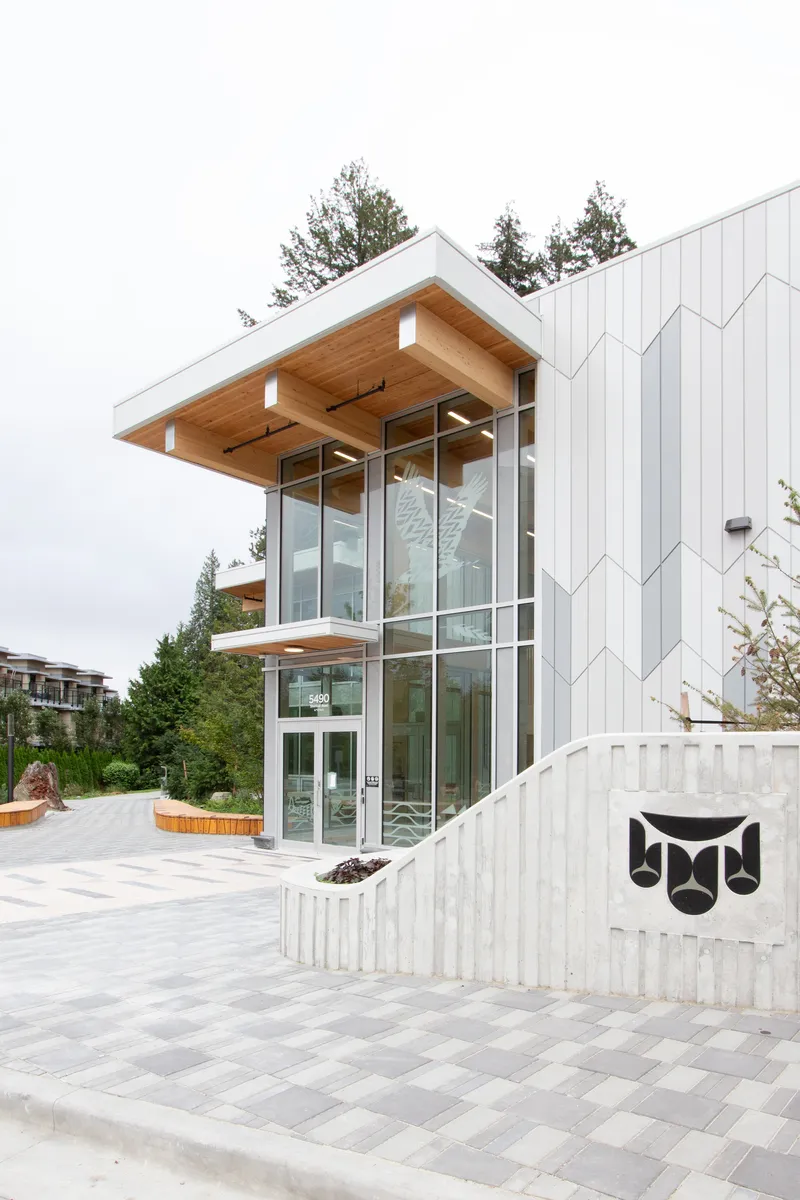 Entry facade with projecting timber soffit and chevron-patterned metal cladding under an overcast sky