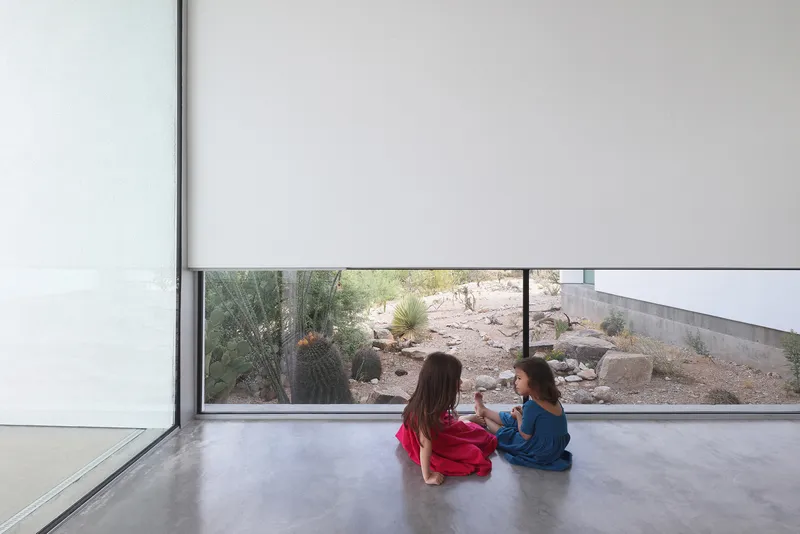 Low horizontal window framing desert landscaping with two children seated on polished concrete floor