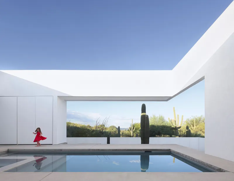 Courtyard pool reflecting white walls and sky with a child running across the deck