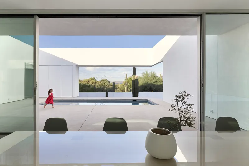 Interior view through dining table toward framed courtyard with pool and child walking past