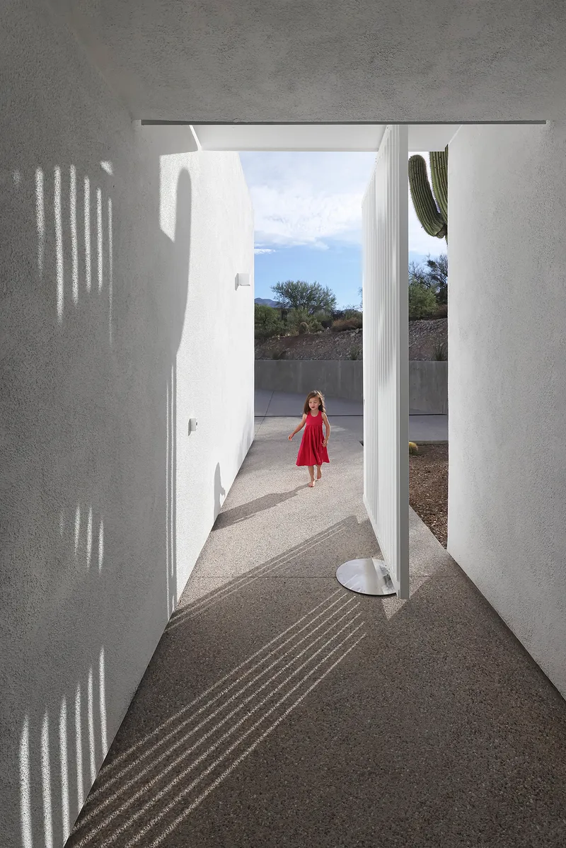 Entry corridor with patterned shadows from perforated screen and child standing in distant courtyard